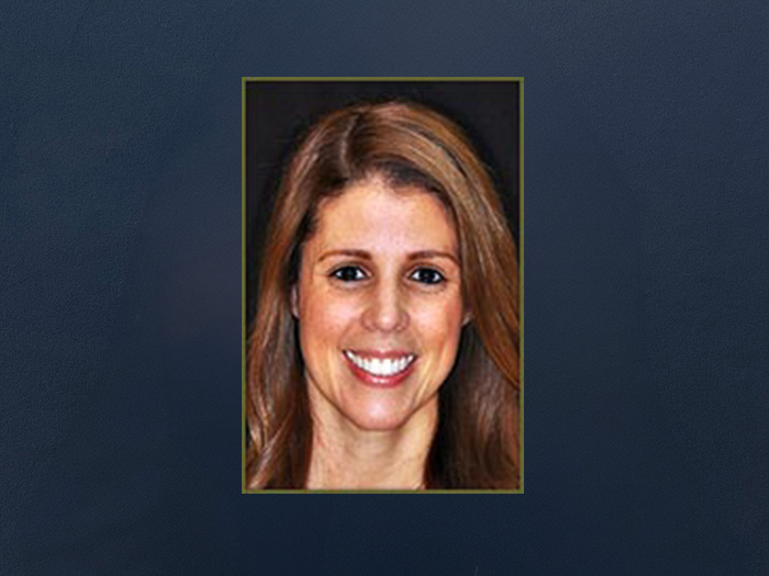 The image is a portrait of a woman with a smile, wearing makeup and a sleeveless top, set against a plain background.