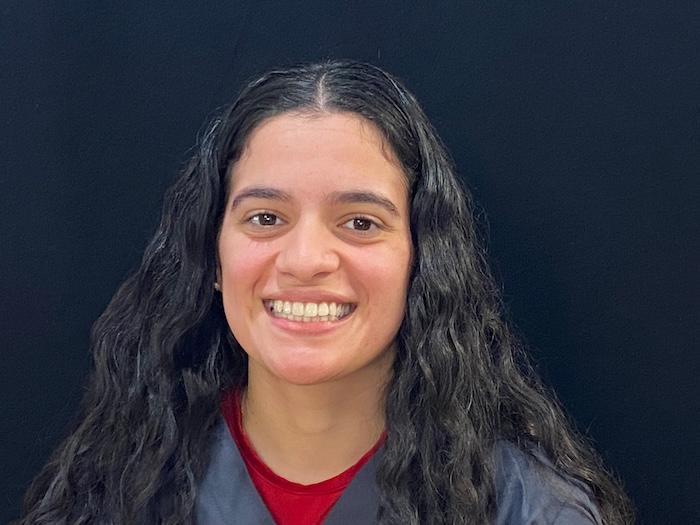 The image shows a person with long hair smiling at the camera against a dark background.