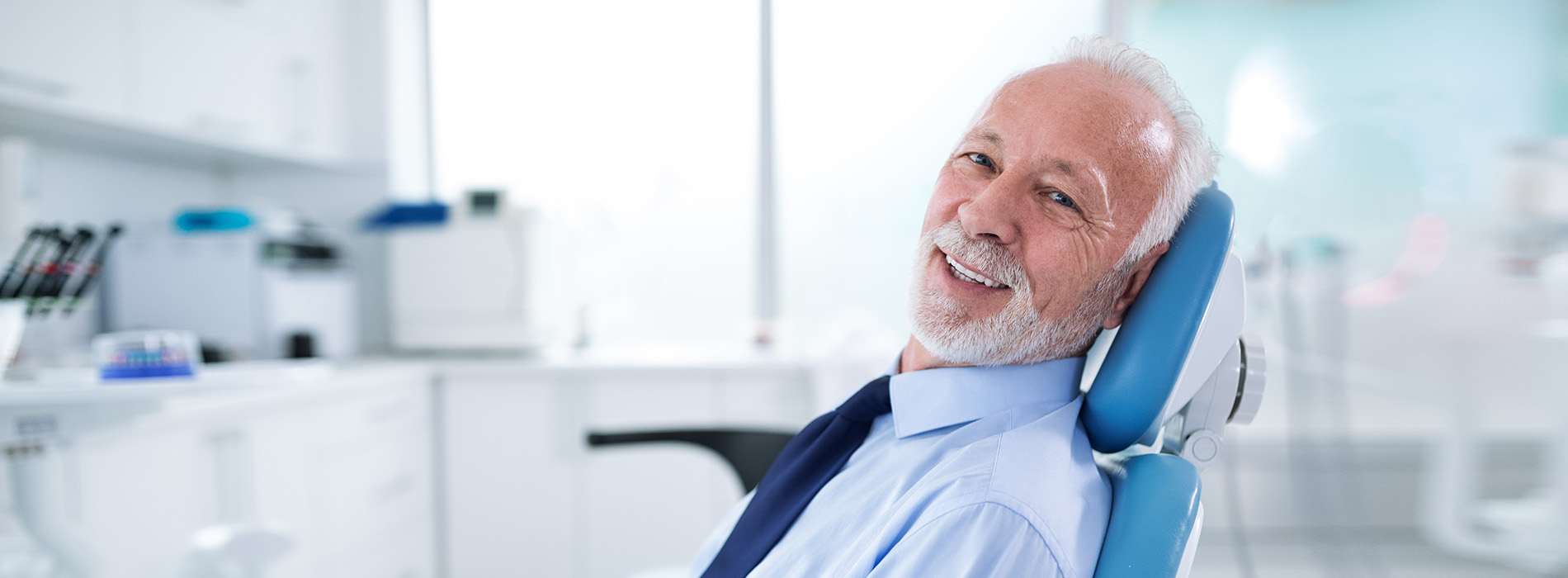 A smiling man sitting in a dental chair, surrounded by dental equipment and instruments.