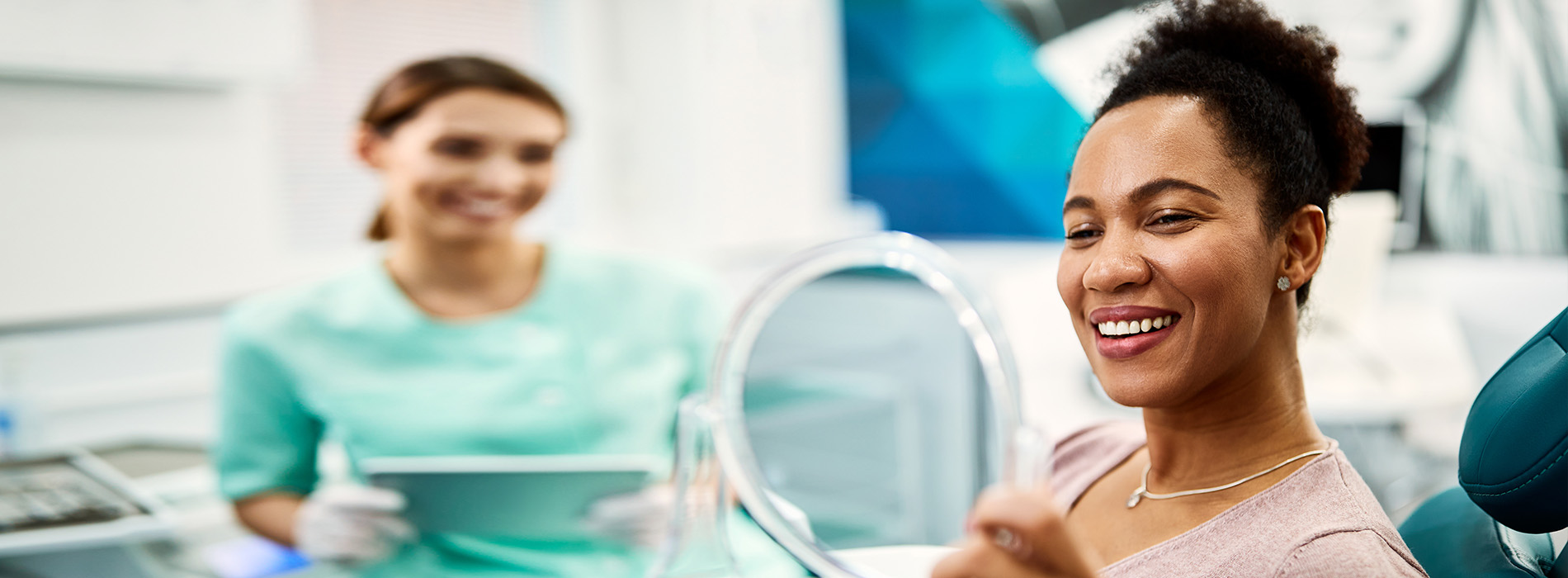 The image shows a woman smiling at the camera while sitting in a dental chair, with another person visible in the background.