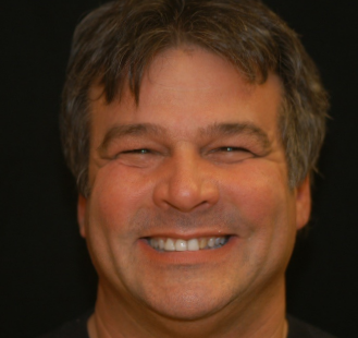 The image features a man with a smiling expression, wearing glasses and a blue shirt, against a dark background.