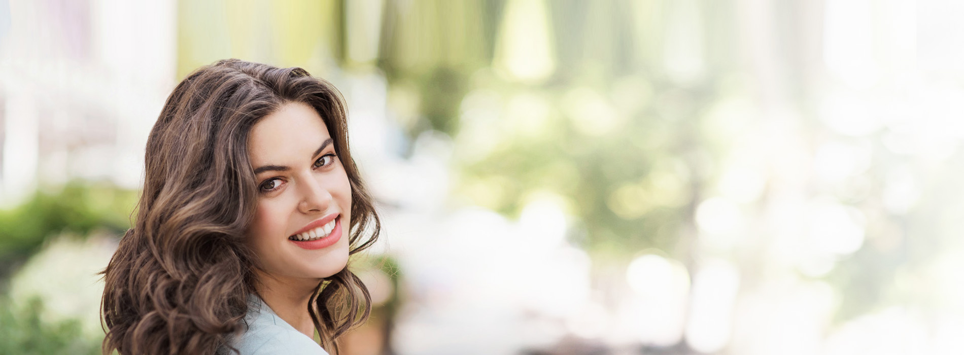 The image is a photograph of a woman with curly hair, smiling and posing for the camera.