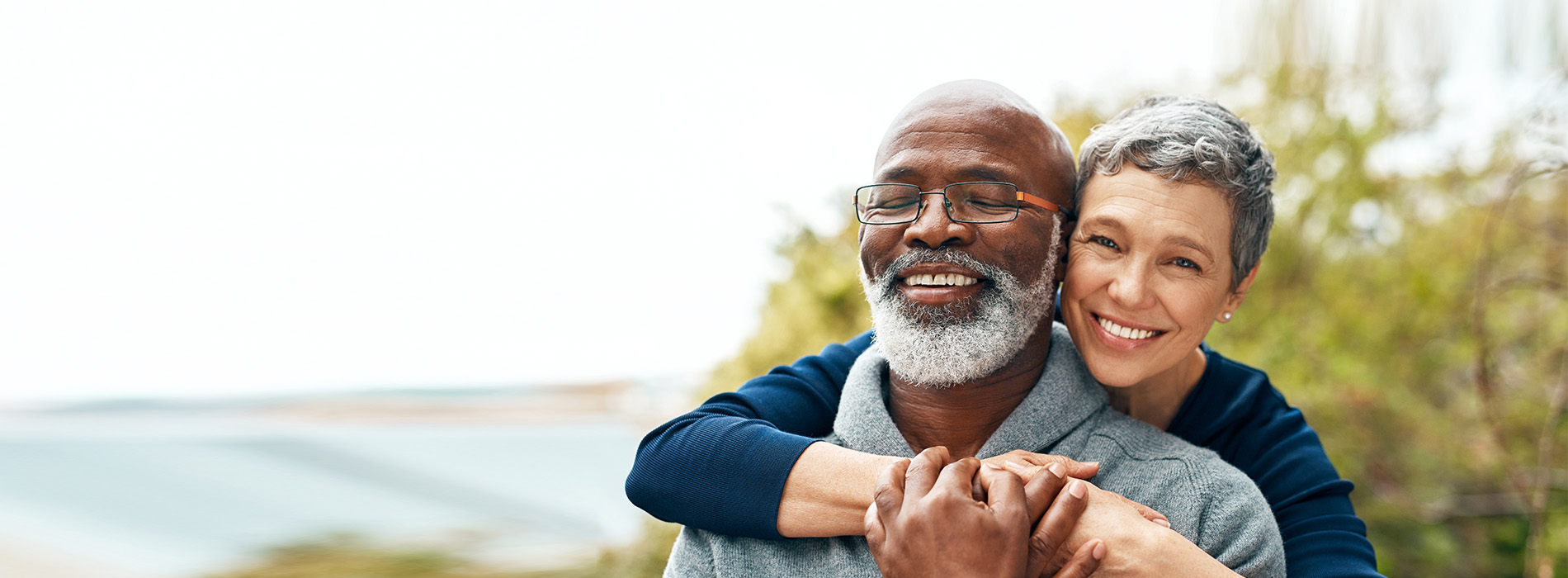 Two elderly adults embracing, smiling and appearing happy together outdoors.