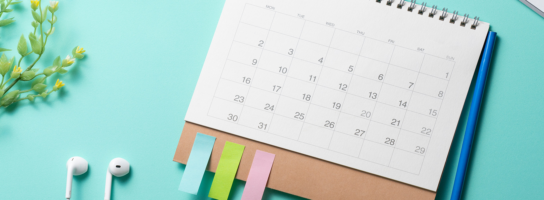 A calendar with a pen and sticky notes on a light blue background, placed next to a smartphone.