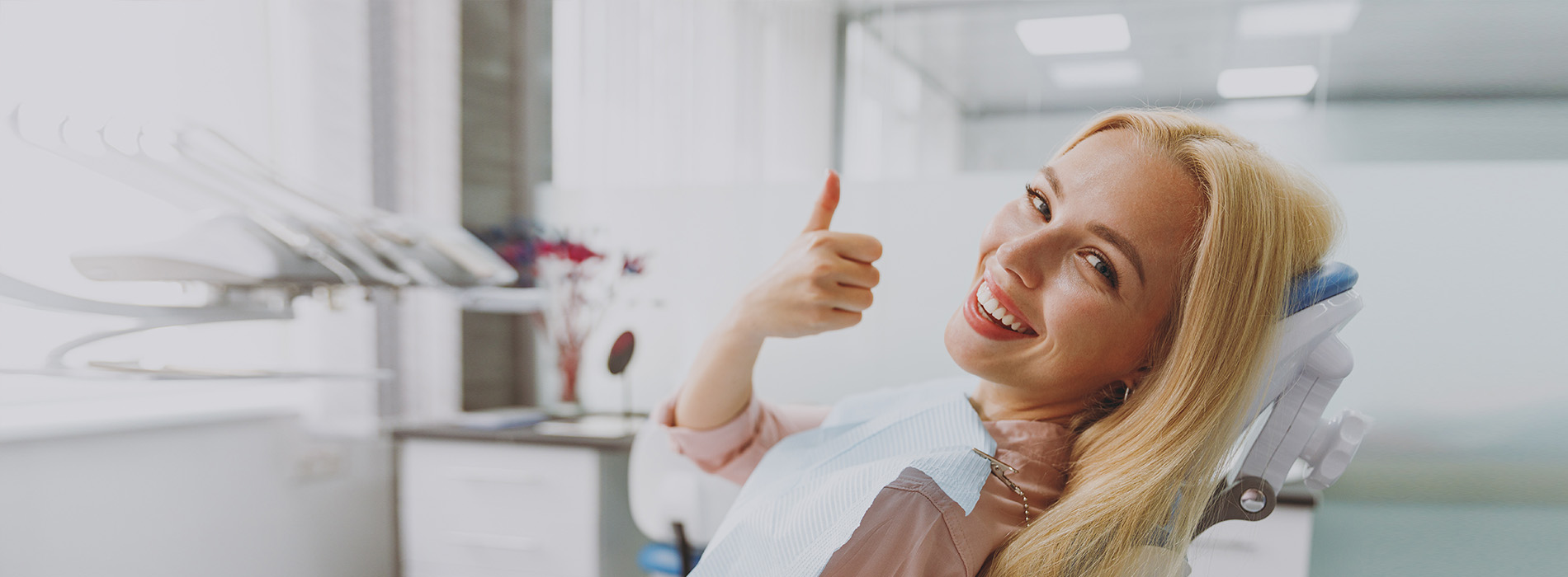 A cheerful woman in a dental office, giving a thumbs-up sign.