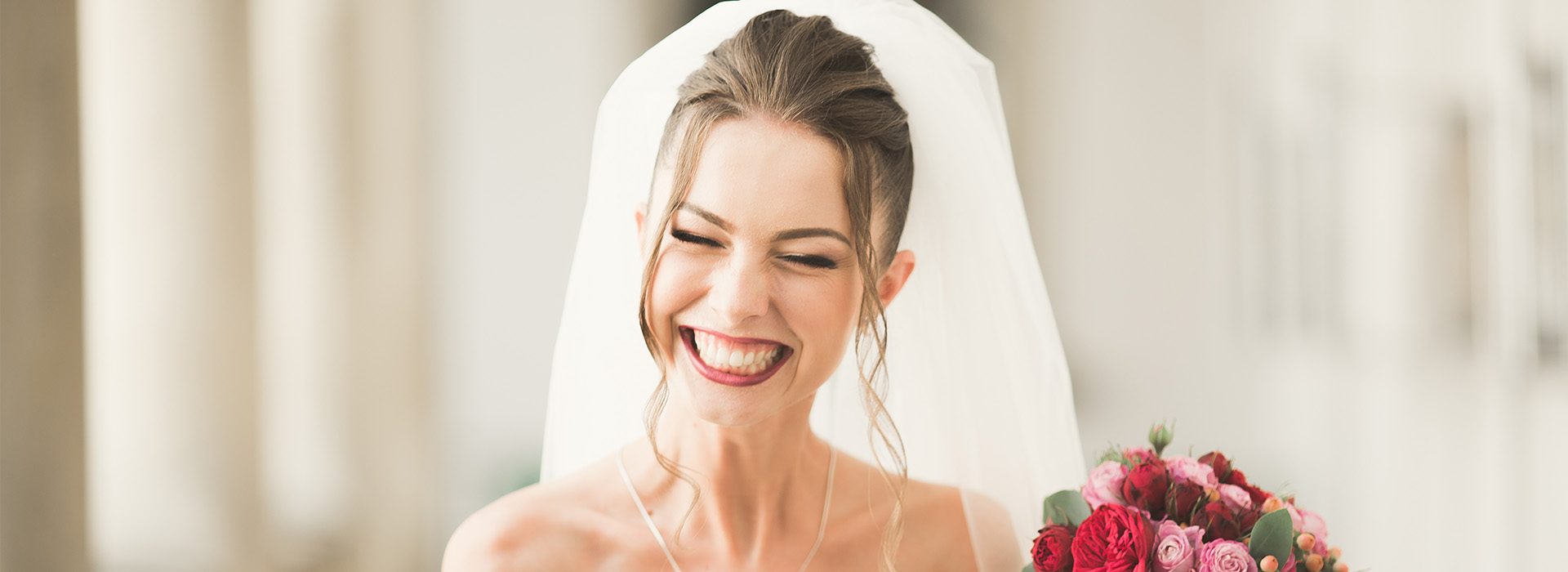 A bride with a radiant smile, wearing a white veil and holding a bouquet of flowers.