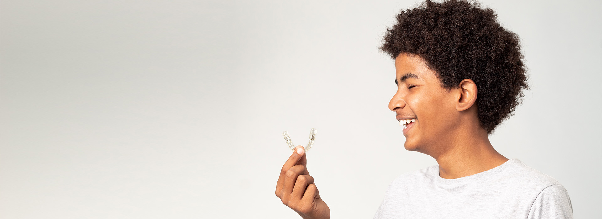 The image shows a young person holding a flower, smiling, with the background blurred to focus on them.