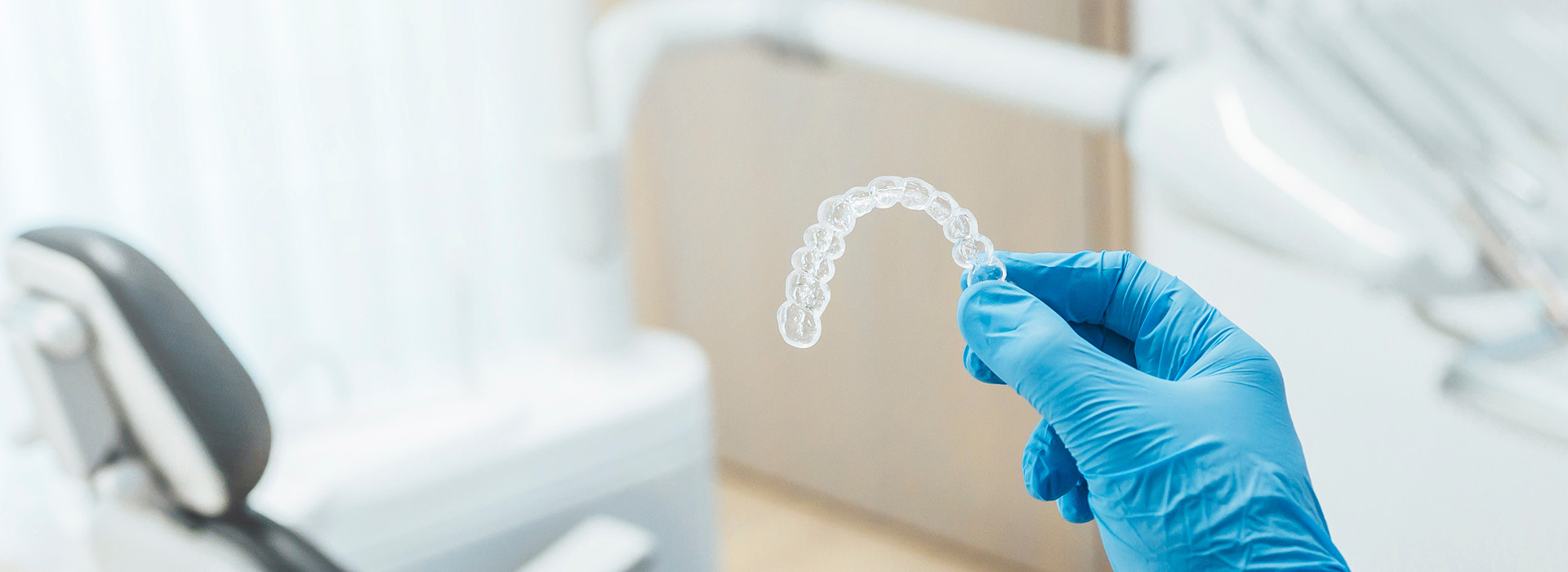 A person in a white lab coat and blue gloves is holding a transparent, plastic dental impression.