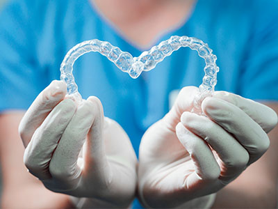 A hand holding a pair of clear braces with a heart shape in the center, symbolizing dental care or love for oral health.