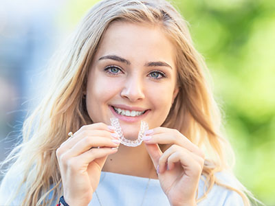 A woman holding a dental appliance, smiling at the camera.