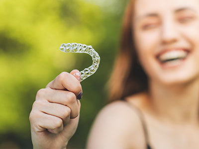 A smiling woman holds a clear plastic dental retainer in her hand.