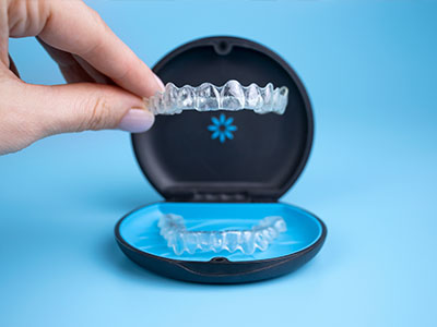 A person s hand holding a blue and black dental appliance, showcasing its design with a clear view of the teeth-like structure within.