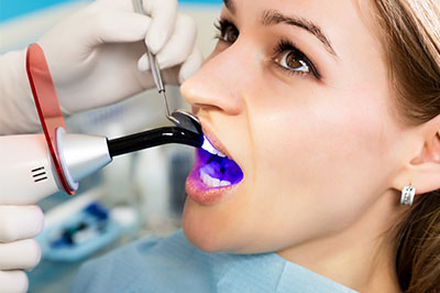 The image depicts a person undergoing dental treatment, with a dentist using an ultrasonic scaler on their teeth.