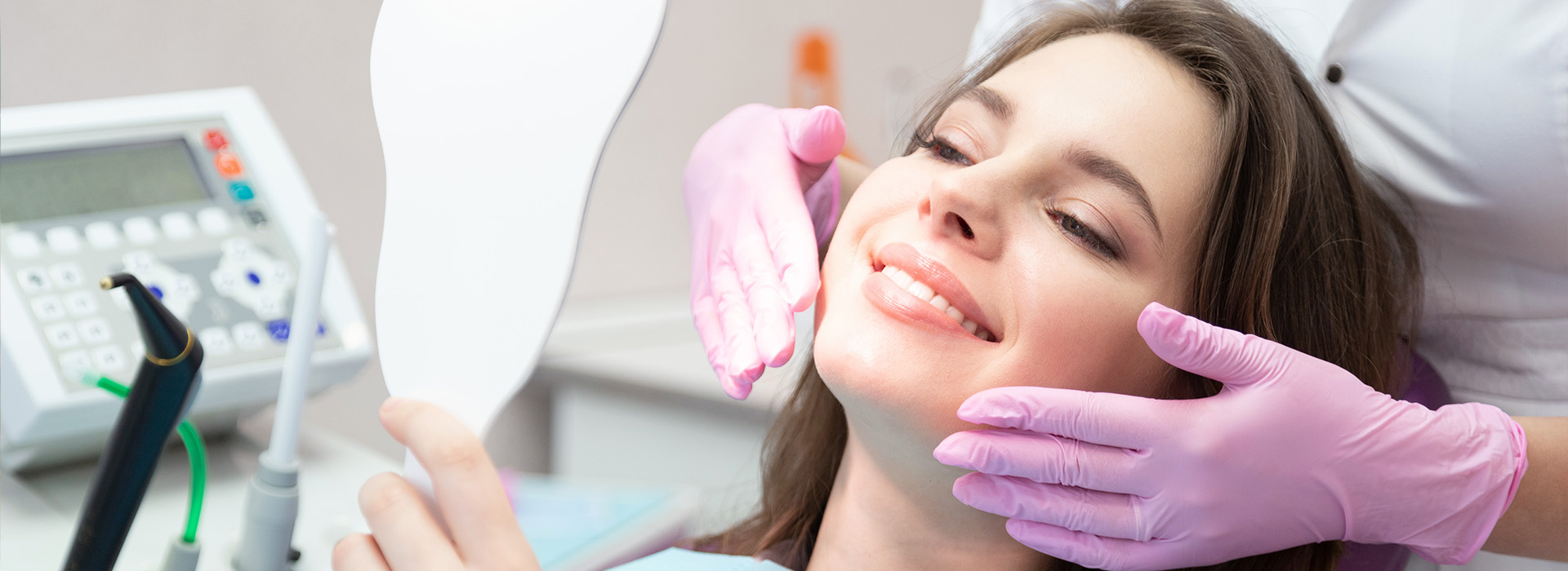 A person receiving dental care, with a dentist holding a mirror to their face and adjusting it.