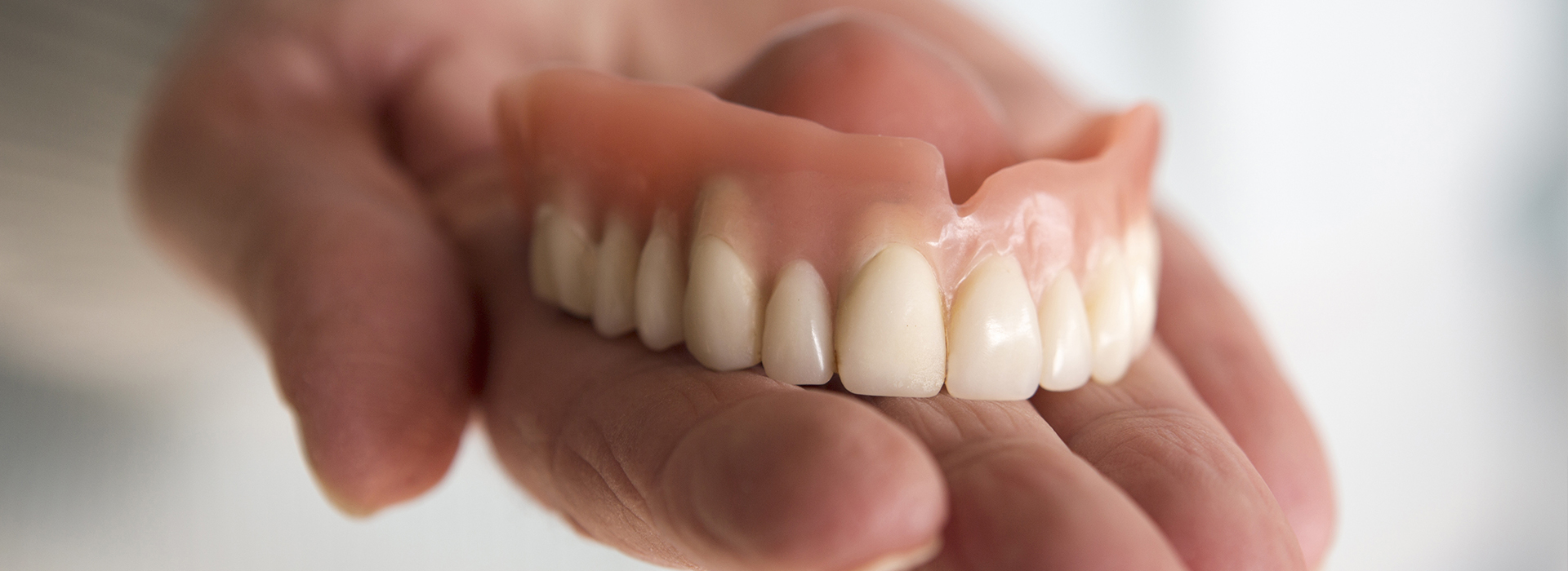 A person s hand holding a set of dentures with visible teeth.