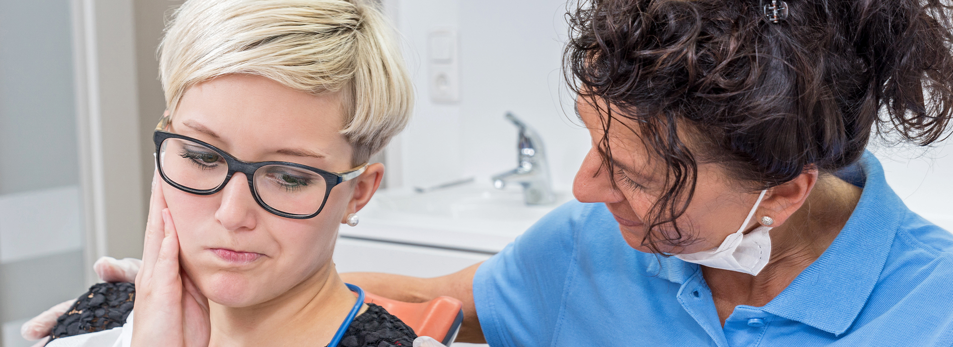 A woman with glasses is receiving dental care from a professional, likely in a dental clinic setting.