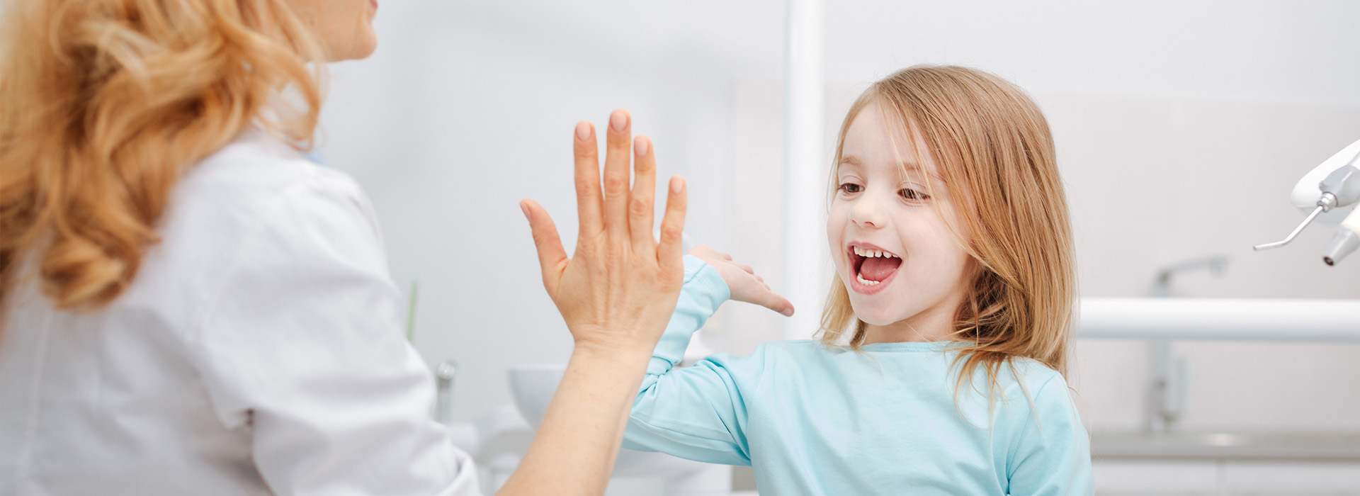 The image features a young girl with a surprised expression, reaching out towards an adult woman who is smiling and has her hand extended. They are in a bathroom setting with a sink visible, and the adult appears to be guiding or assisting the child.