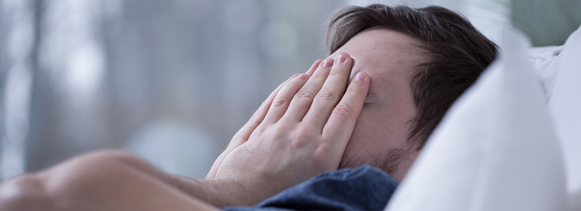 The image shows a person lying in bed with their hands covering their face, possibly in a state of surprise or shock.