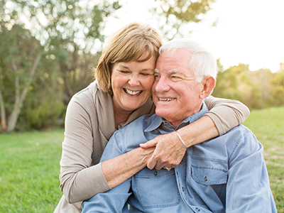 The image depicts an older couple, a man and a woman, sharing a warm embrace while seated outdoors.