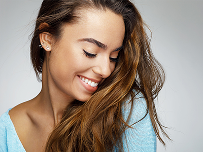 The image is a close-up portrait of a person with long hair, smiling gently at the camera.