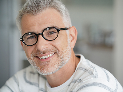 A man with gray hair, wearing glasses and a white shirt, smiling at the camera.