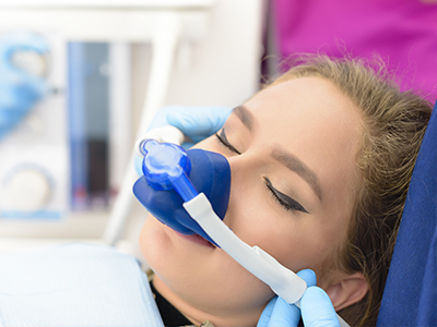 A woman receiving medical treatment, with an oxygen mask on her face and a nurse attaching a device to her mouth.